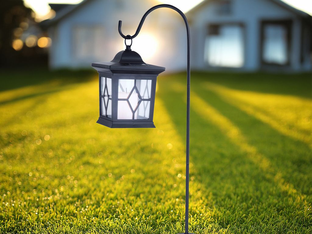 A solar lantern is mounted on a pole in a grassy yard with houses in the background during sunset.