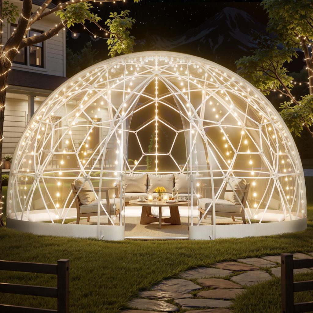 A transparent geodesic dome tent set up in a backyard at night, illuminated by string lights, with outdoor furniture inside.