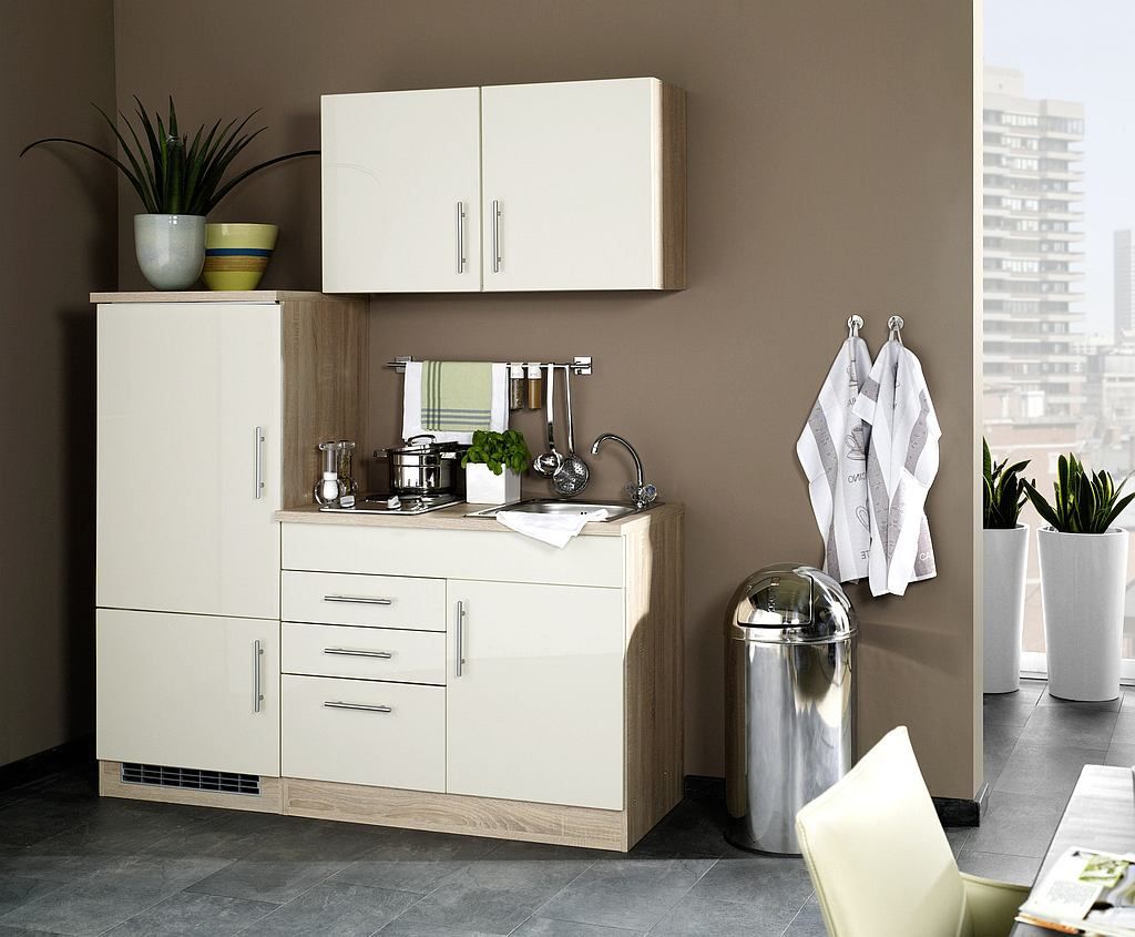 A compact kitchen unit with cabinets, sink, and appliances, set against a brown wall with a window view in the background.