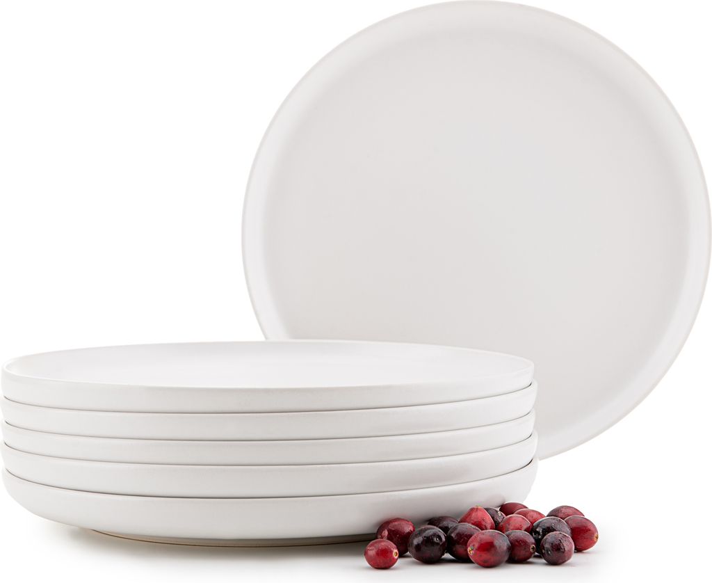 A stack of white ceramic plates with a few cranberries in the foreground.