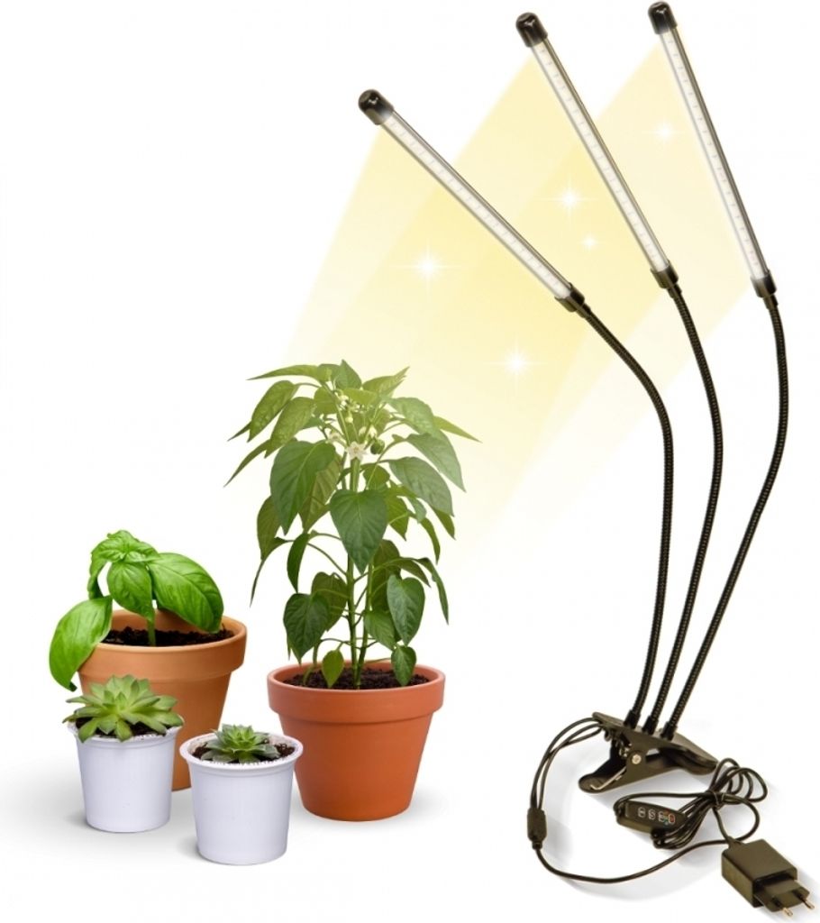 A plant grow light with three adjustable LED heads is positioned next to several potted plants on a white background.