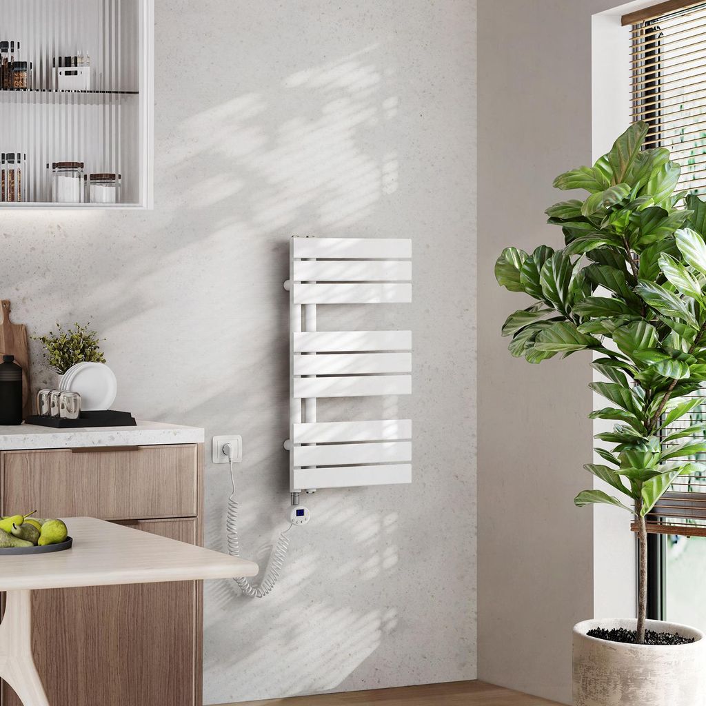 A modern kitchen or bathroom setting with a white electric towel warmer mounted on a light gray wall, next to a large potted plant and a wooden cabinet.