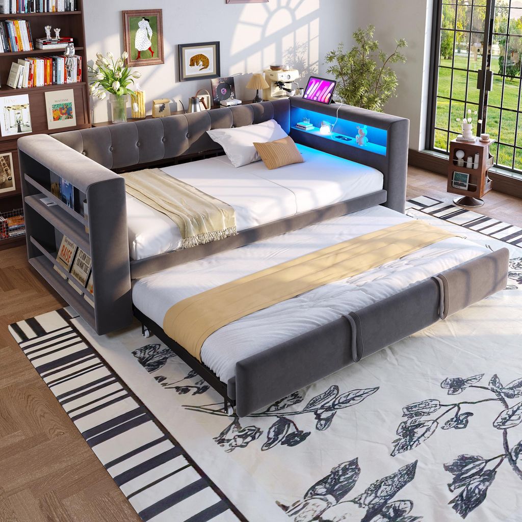A gray upholstered daybed with a pull-out trundle bed, featuring built-in shelving and LED lighting.