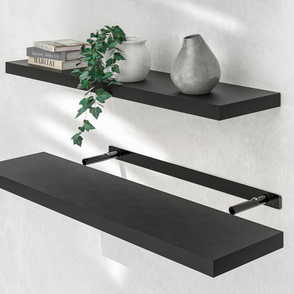 Two black floating shelves mounted on a white wall. The top shelf has books, a plant, and a vase. The bottom shelf is empty.