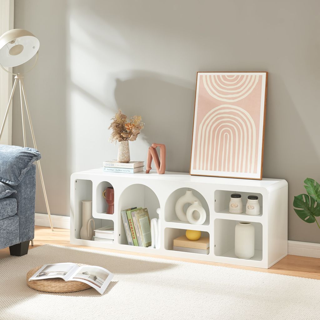 A white TV stand with various decorative items and books is shown in a living room setting.