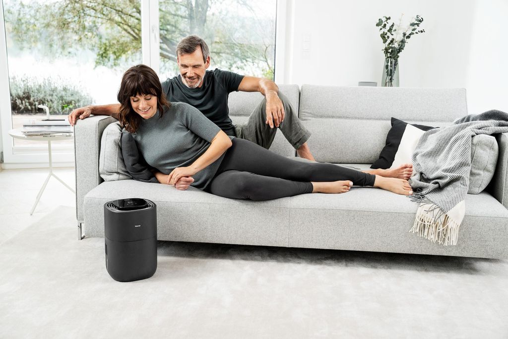 A couple relaxing on a couch with an air purifier in the foreground.