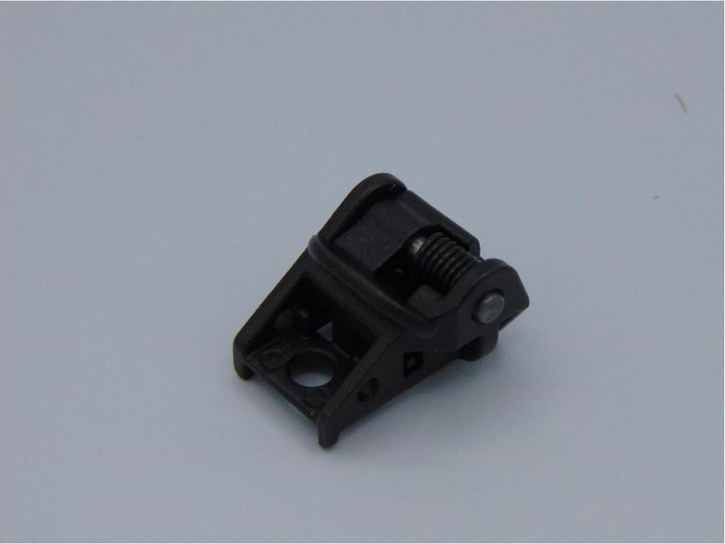 A black plastic part with a spring mechanism, likely a component for a power tool, is shown against a plain light gray background.