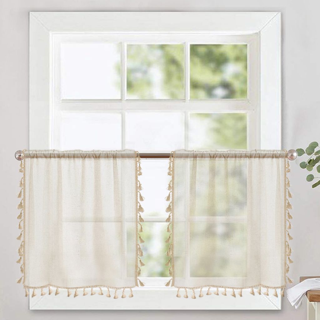 Two sheer cream-colored cafe curtains with tassels hanging on a window.