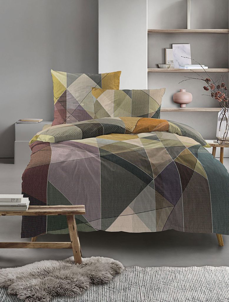 A bed with geometric patterned bedding is shown in a room with minimalist decor.