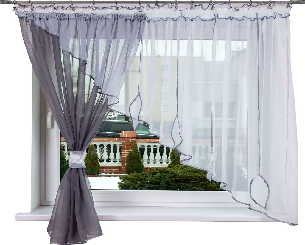 A window with curtains and a view of a garden and building.
