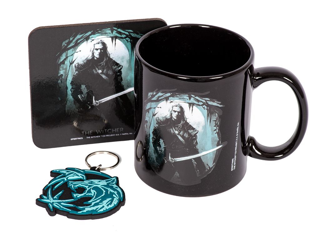 A black mug, a square coaster, and a keychain are displayed together on a white background. All items feature artwork from The Witcher, including a depiction of Geralt of Rivia and the Wolf School medallion.