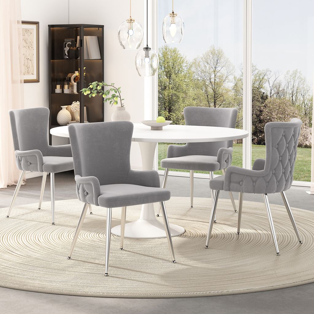 A dining set with four gray velvet chairs around a white round table, set in a well-lit room with a large window overlooking a garden.