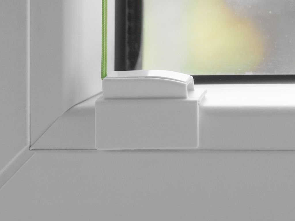 A close-up view of a white window fitting, likely a mounting bracket or clamp, attached to a white window sill.