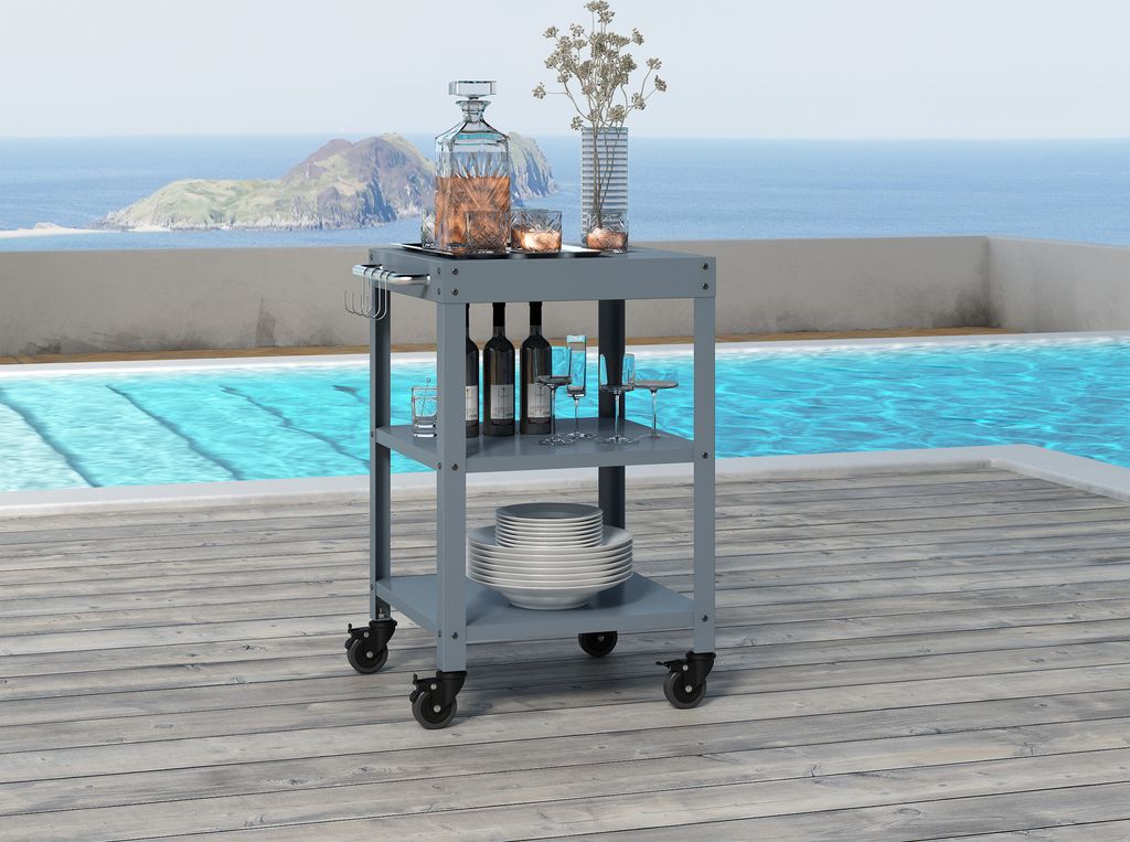 A dark gray serving cart is placed on a wooden deck next to a swimming pool with a view of the ocean and islands in the background.