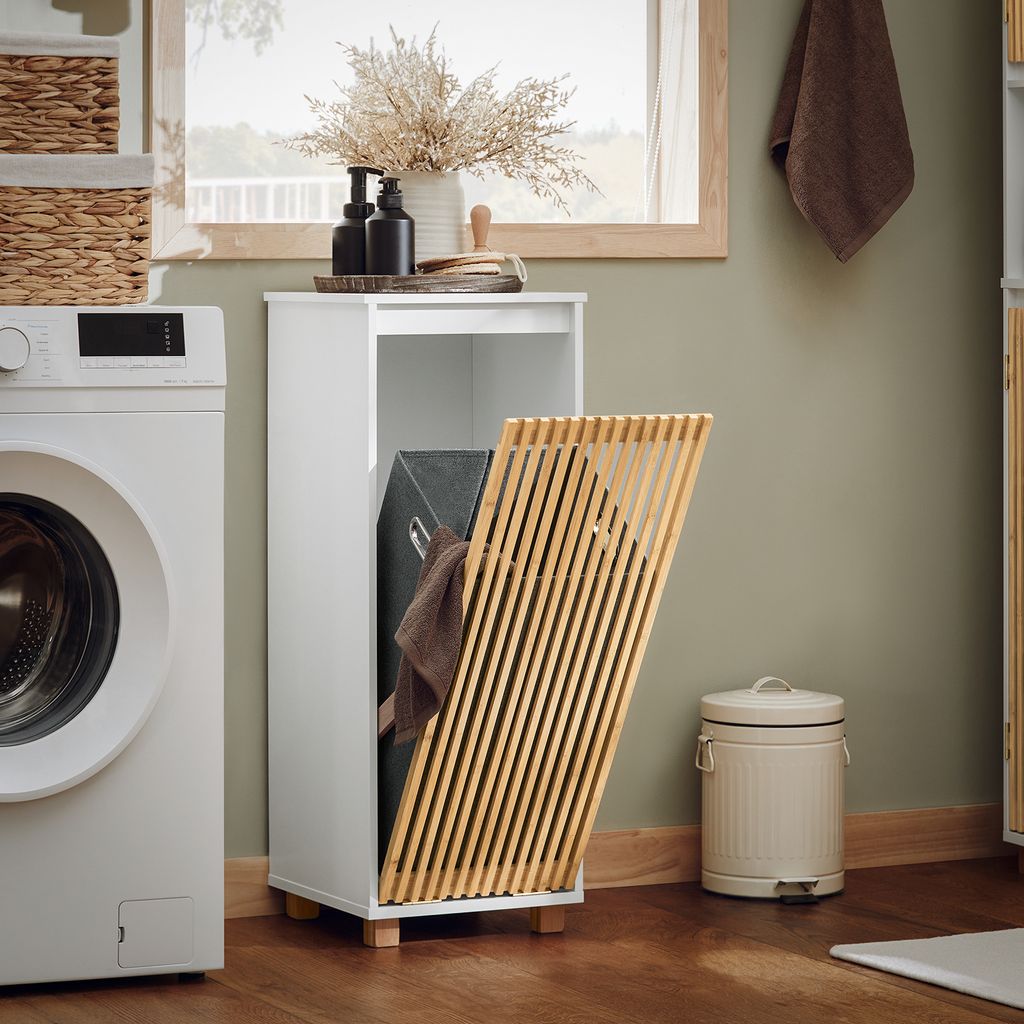 A laundry room scene with a washing machine, a white cabinet with a slatted door, a laundry basket inside, and a trash can.