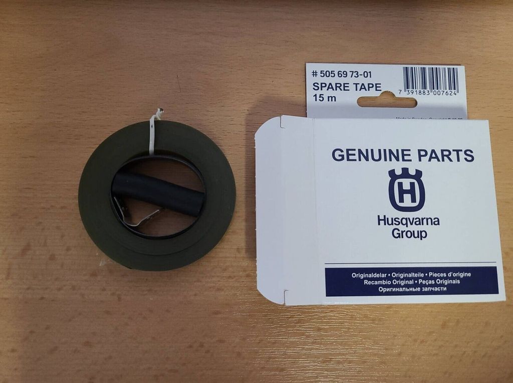 A roll of green tape and a white box of Husqvarna genuine parts are placed on a wooden surface.