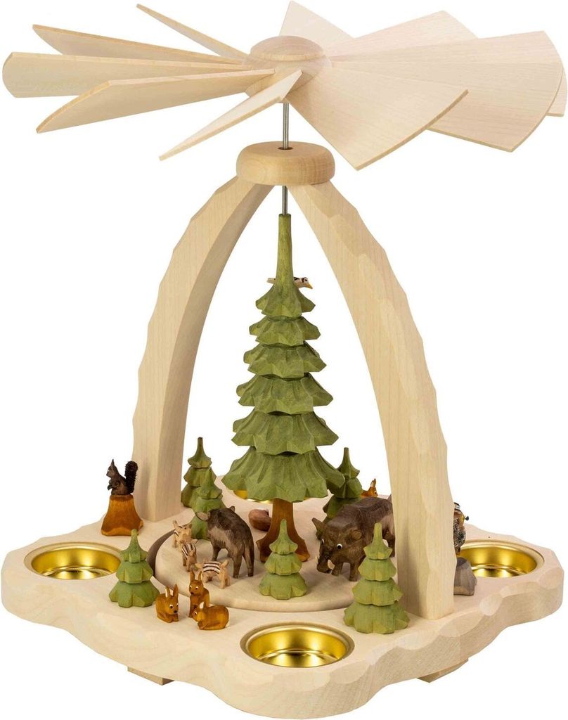 Ein hölzernes Weihnachtspyramidenmodell zeigt eine winterliche Waldszene mit Tieren und Bäumen während oben ein Flügelrad die Pyramide ziert und vier Kerzenhalter am Rand platziert sind