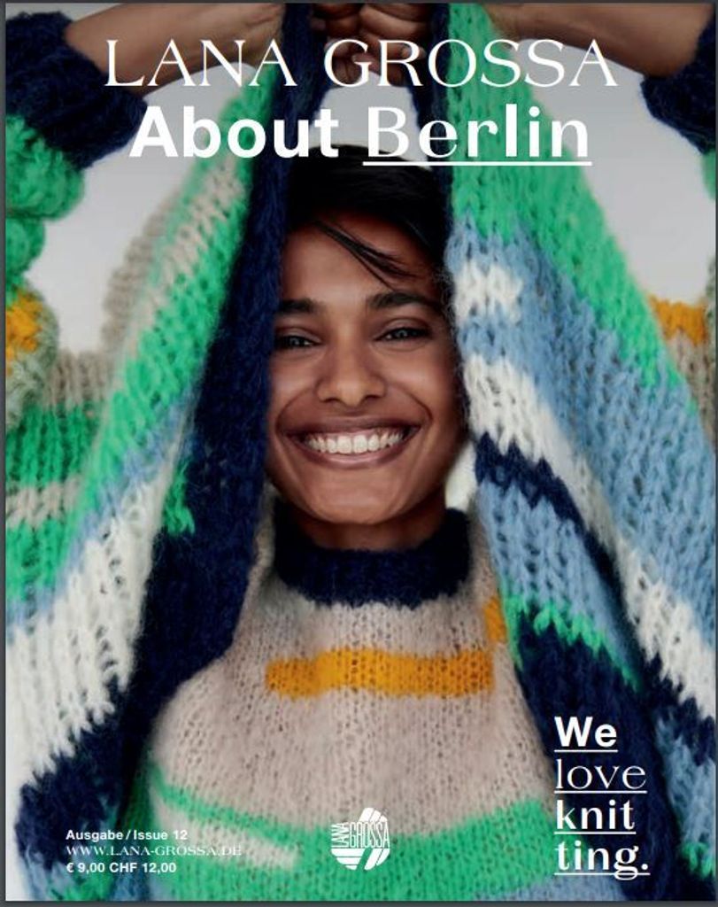 A woman smiling and holding up a colorful knitted sweater.