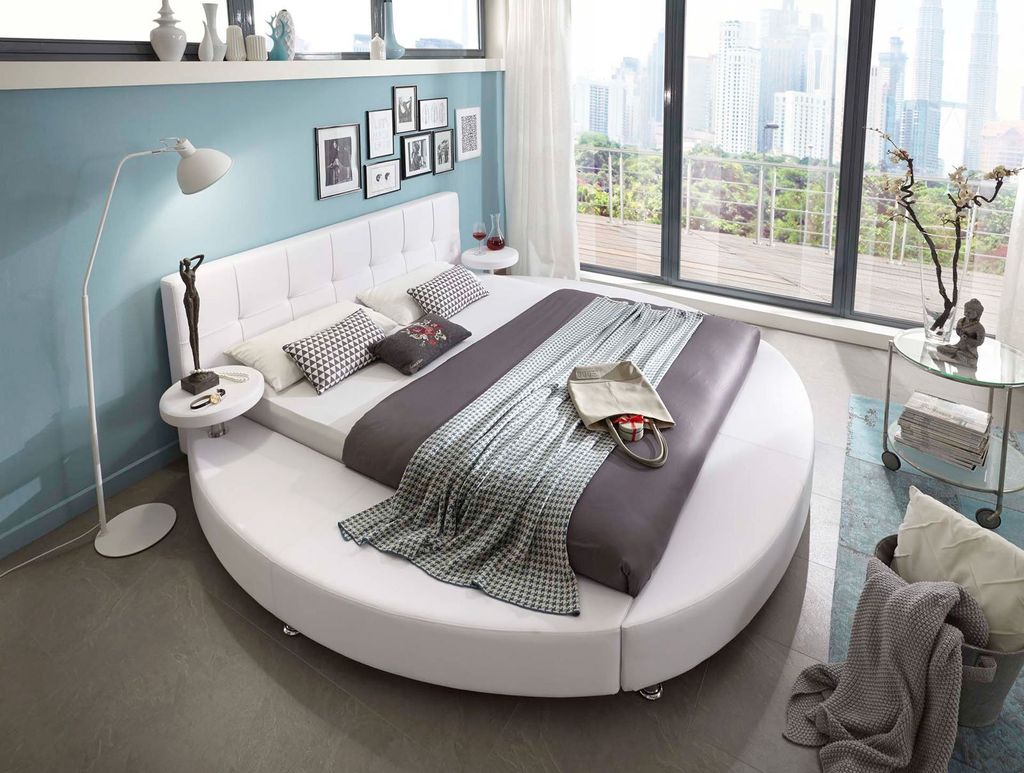 A modern bedroom with a large round bed, floor lamp, and a city view from the window.