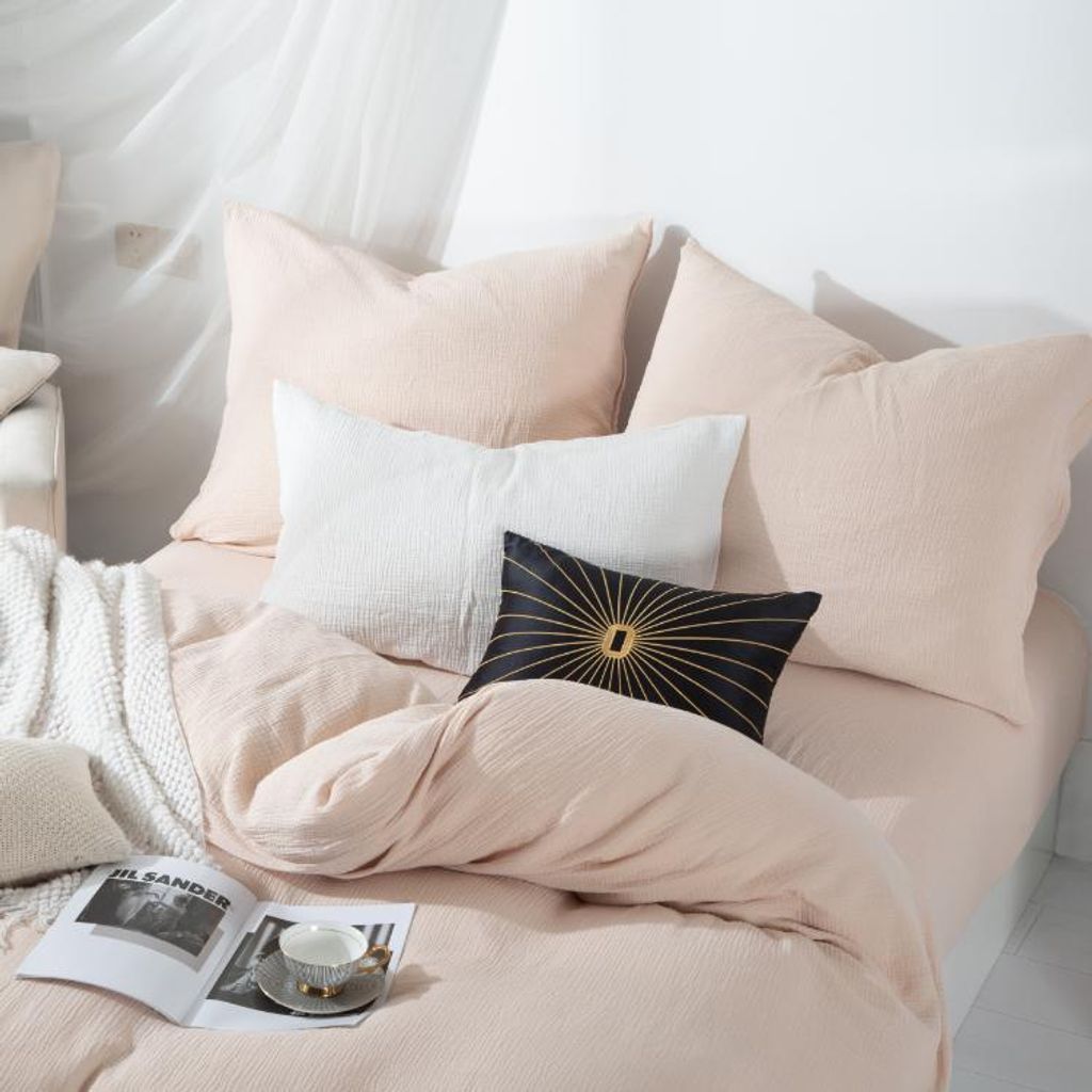 A neatly made bed with several pillows and a duvet, a book and a teacup are placed on the bed.
