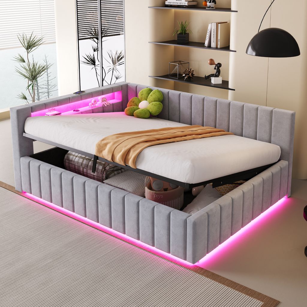 A modern bedroom with a grey upholstered daybed featuring pink LED lighting and storage underneath. A green floral pillow and a brown blanket are on the bed.