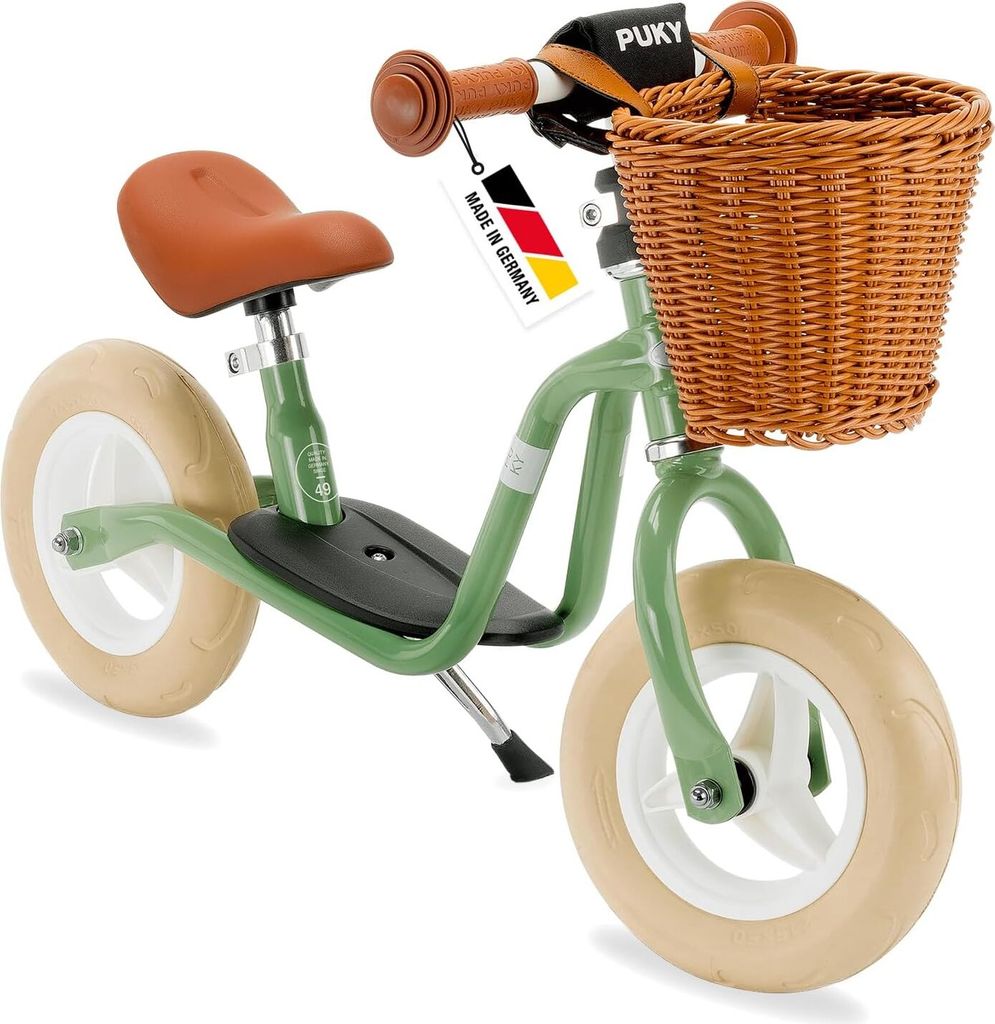 A green Puky balance bike with a wicker basket and brown seat and handlebars, shown against a white background.