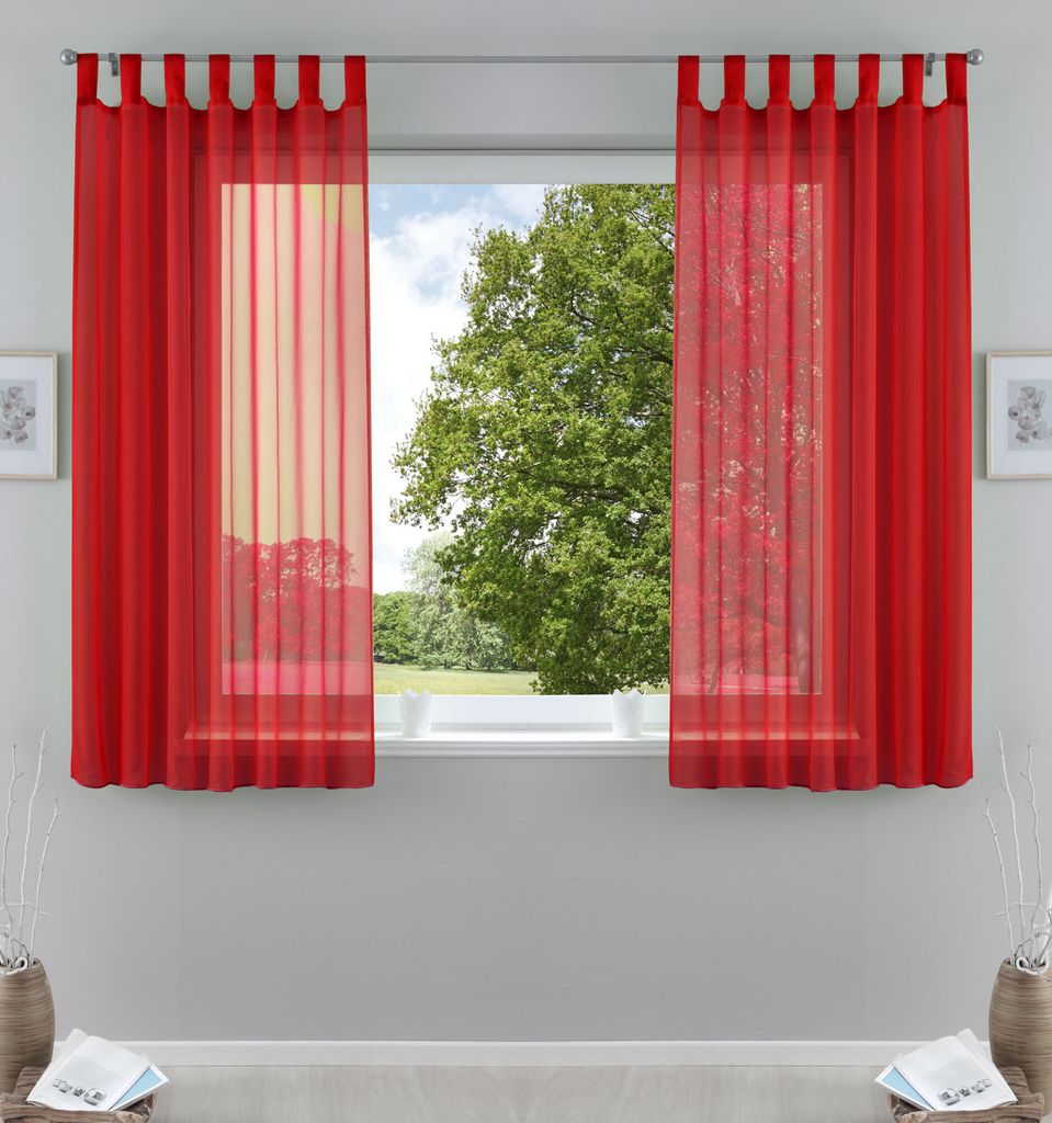 A window with red sheer curtains, showing a green tree and blue sky outside.