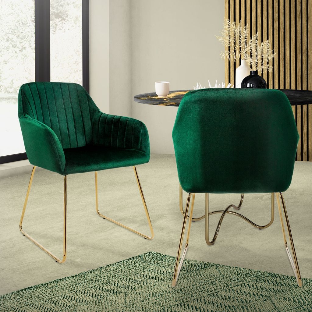 Two green velvet dining chairs with gold legs are placed around a dark marble-topped dining table in a well-lit room.