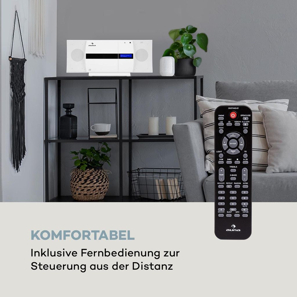 A compact stereo system is displayed on a shelf in a living room setting, with a remote control in the foreground.
