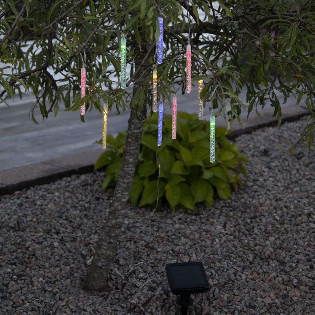 Solar-powered LED icicle lights hanging from a tree branch in a garden setting.