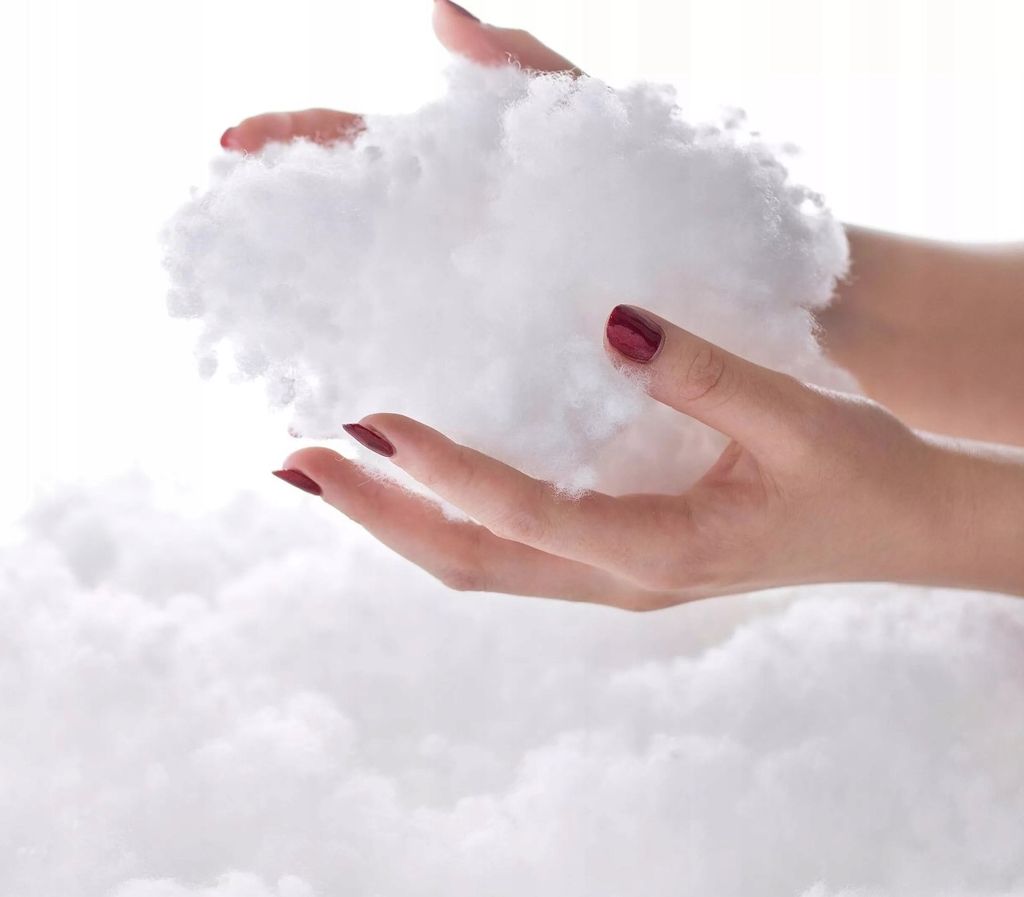 Hands holding a pile of white fluffy material, likely stuffing or batting, against a white background.