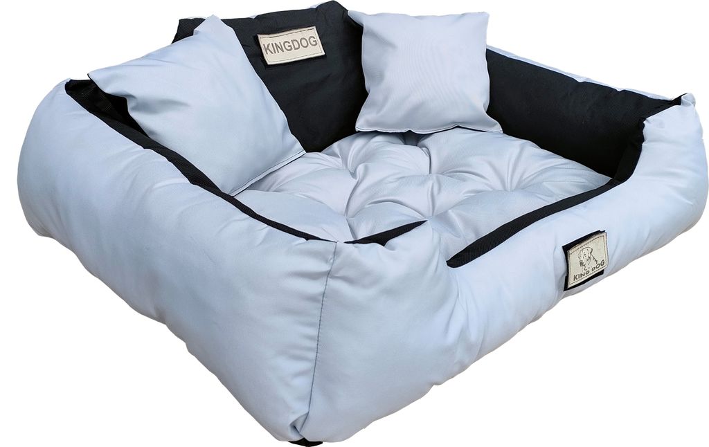 A light gray dog bed with black accents and two small white pillows.