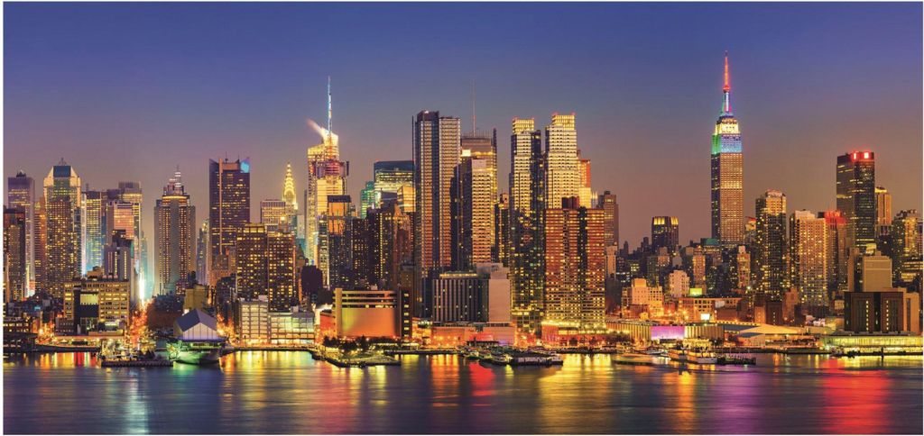 A panoramic nighttime view of a city skyline with illuminated skyscrapers and their reflections in the water.