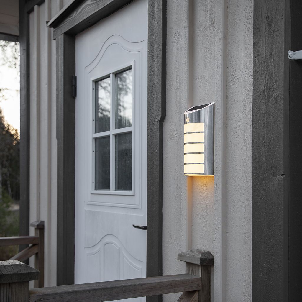A solar-powered LED wall light mounted on the exterior wall of a house next to a white door.