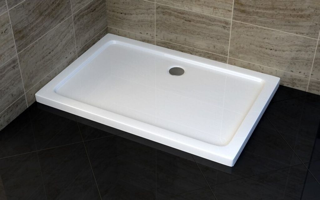A white rectangular shower tray is shown in a bathroom setting with dark tiled flooring and beige tiled walls.