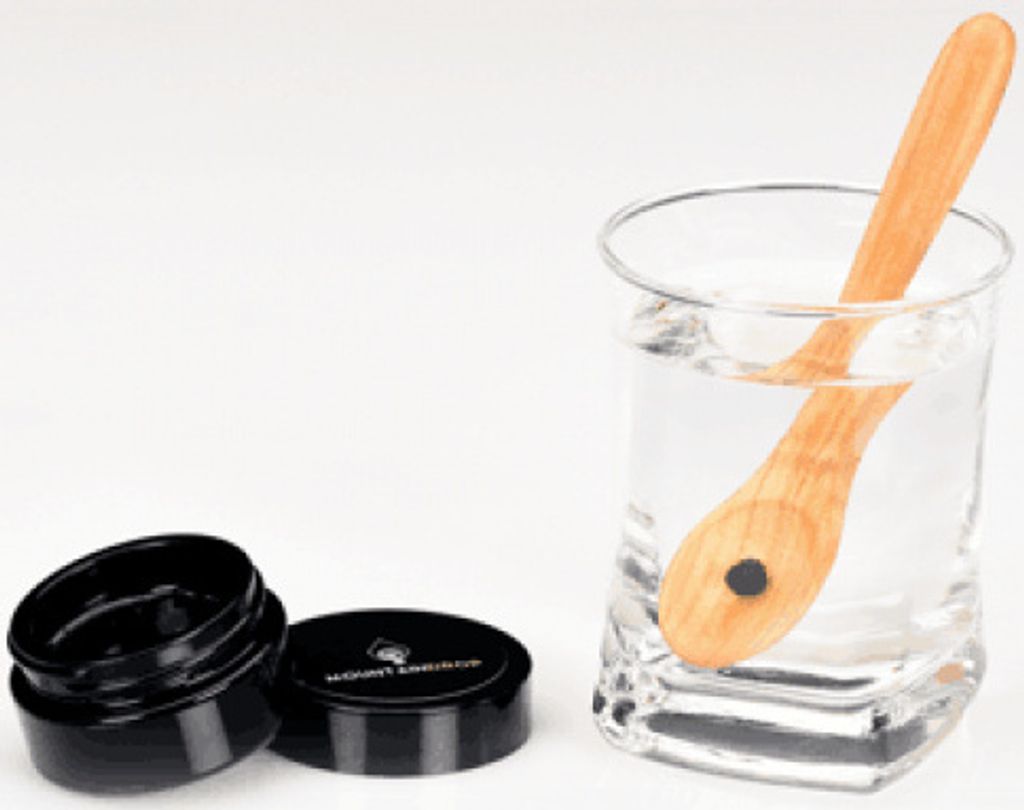 A wooden spoon in a glass of water next to an open container of Shilajit.