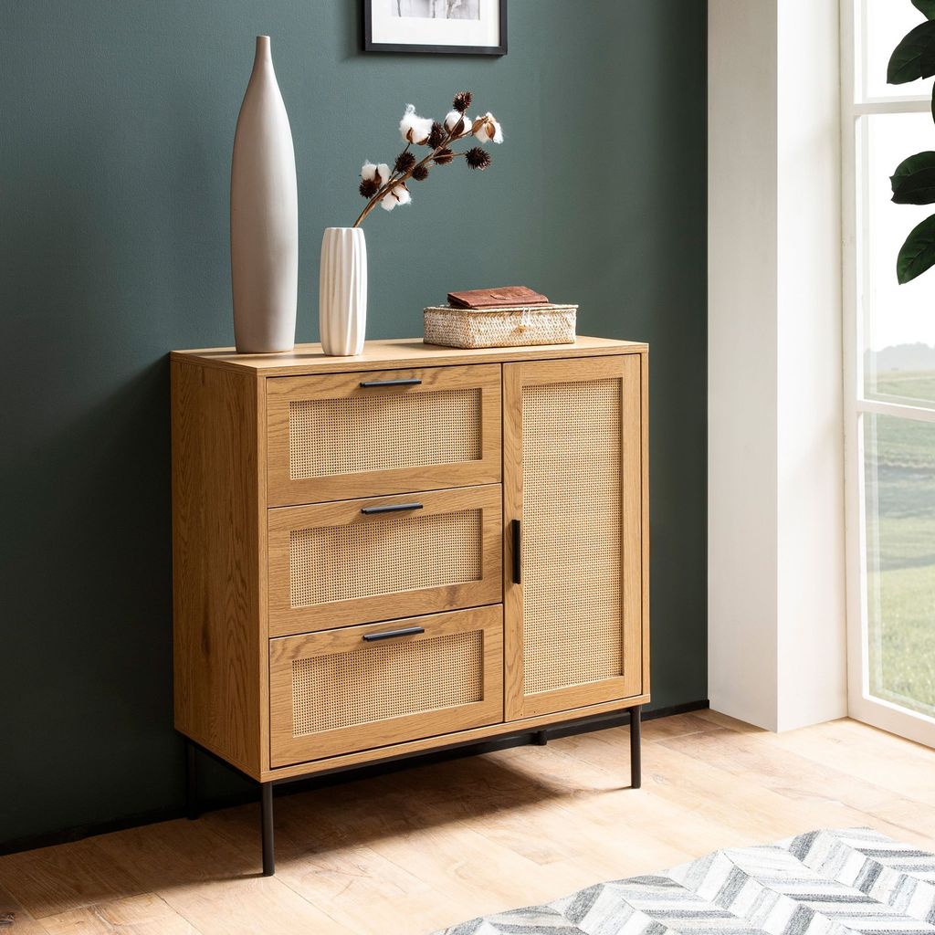A modern wooden sideboard with rattan accents is shown in a room with a teal wall and a window.