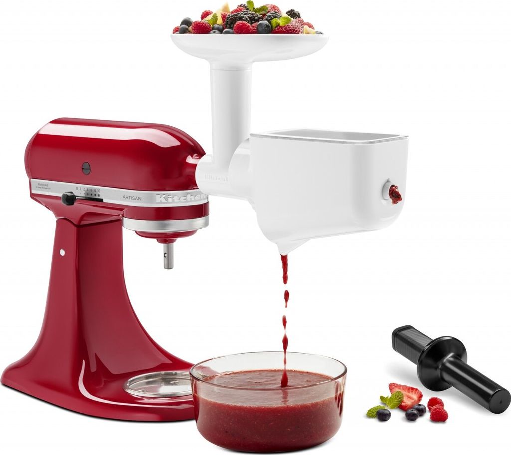 A red KitchenAid stand mixer with a white food grinder and strainer attachment, processing berries into juice. A glass bowl collects the juice, and a black tamper is shown next to some berries.