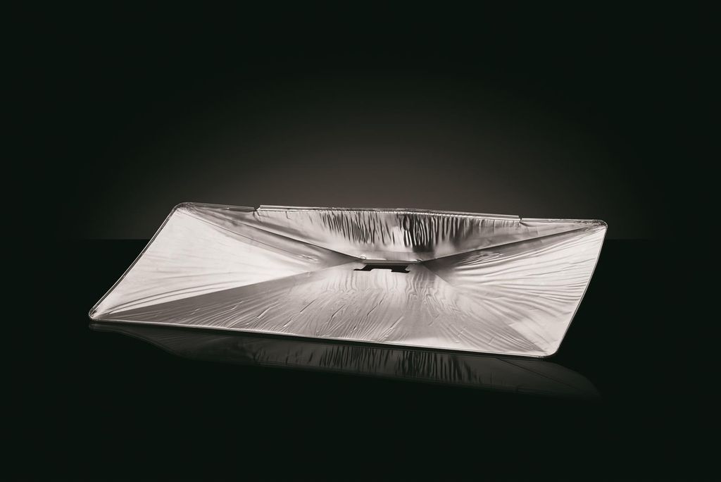 A silver-colored grease tray is shown on a reflective black surface with a dark background.