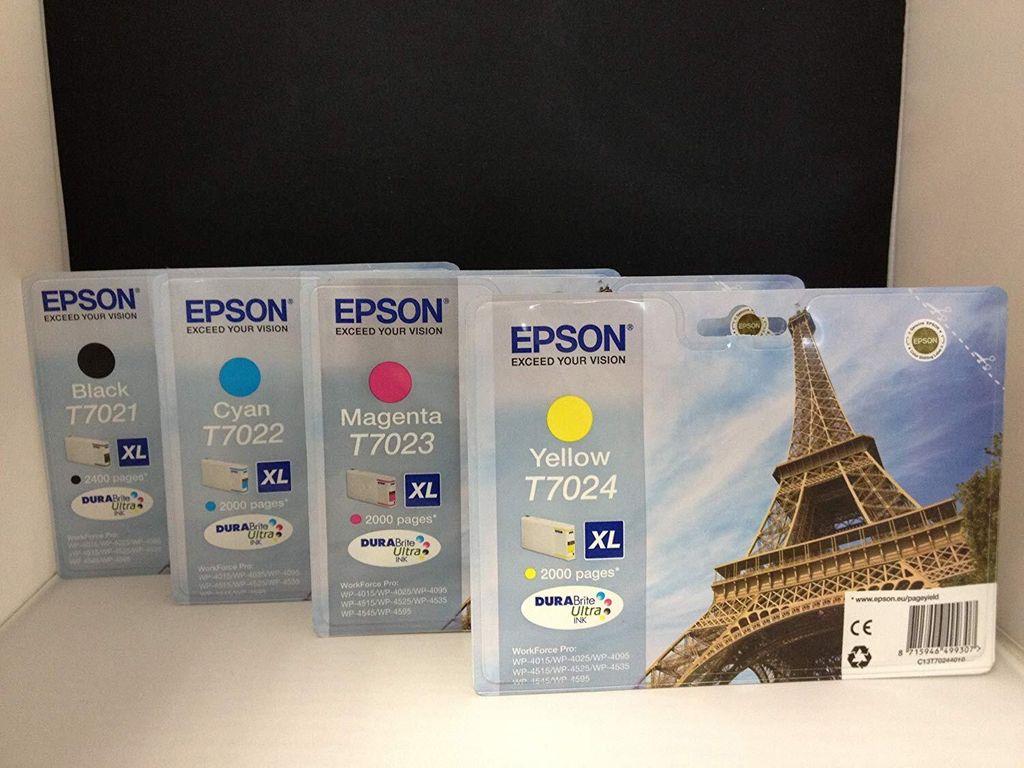 Four Epson ink cartridges are displayed in their packaging, with a picture of the Eiffel Tower on the largest package.