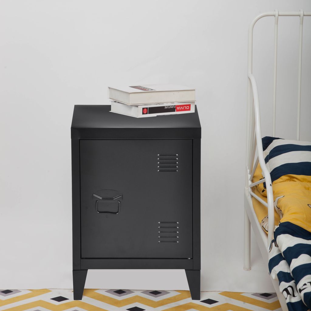 A black metal nightstand with a door and two books on top, placed next to a white metal bed frame.