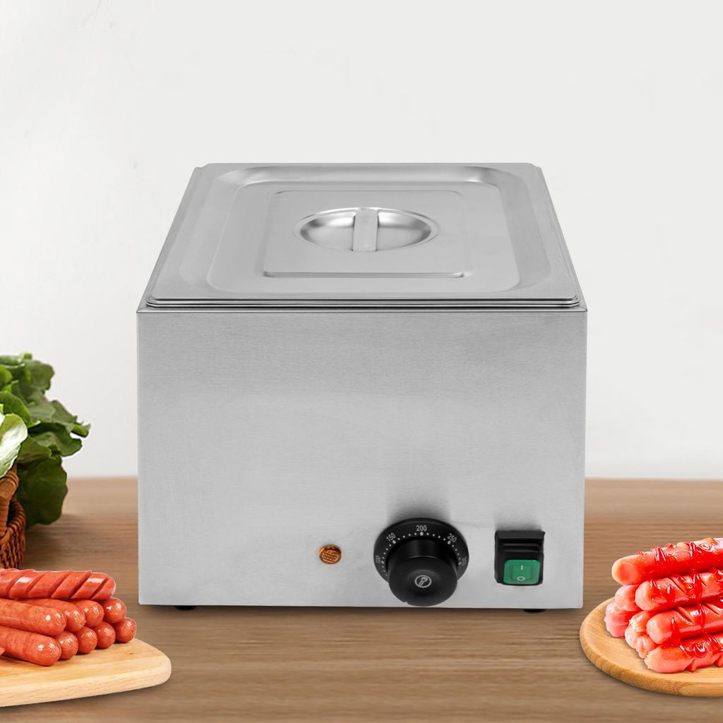 A stainless steel electric sausage warmer with a knob and a switch on the front, placed on a wooden surface. There are sausages on a cutting board to the left and right of the warmer.