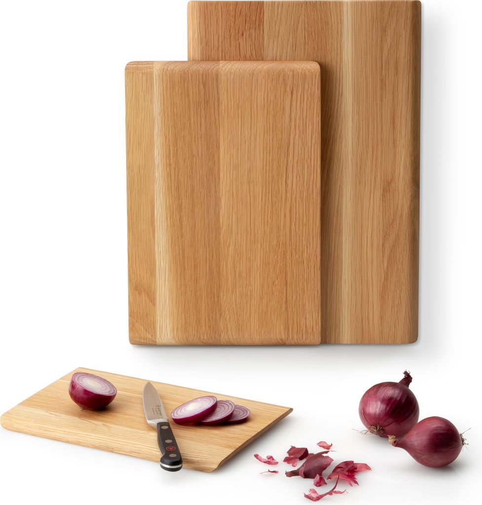 Two wooden cutting boards are shown, one behind the other. In the foreground, a smaller cutting board has a knife, sliced red onion, and a whole red onion on it. Two whole red onions and some onion peels are on the surface next to the smaller cutting board