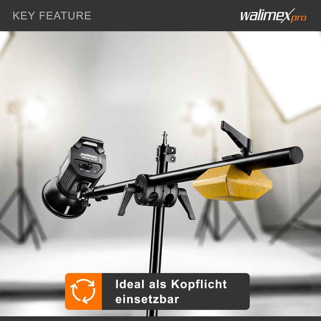 A studio lighting stand with a light attached and a counterweight, set up in a studio environment with softboxes in the background.