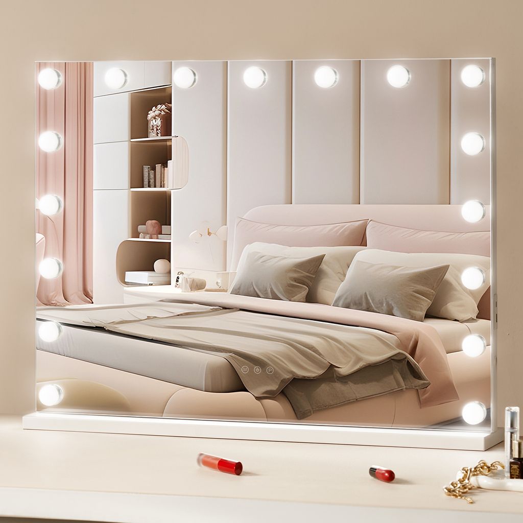 A vanity mirror with lights is placed on a dresser in front of a bed.