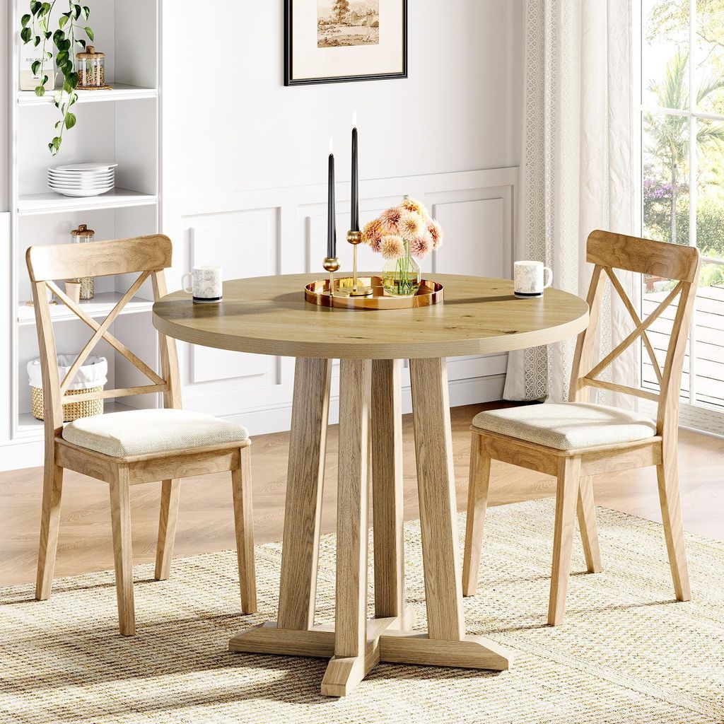 A round wooden dining table with two chairs in a well-lit room, with a bookshelf in the background.