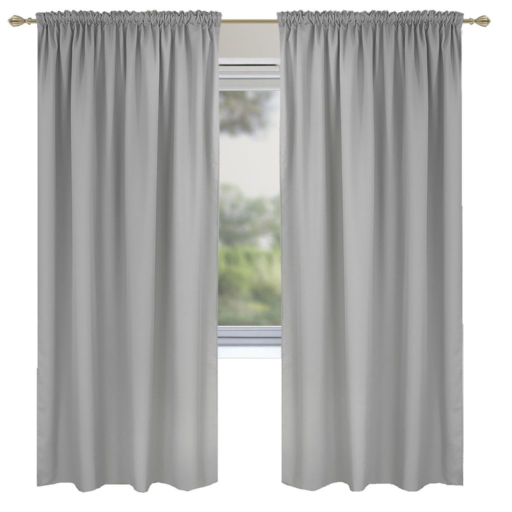 Two light gray curtains hanging on a curtain rod in front of a window with greenery visible outside.