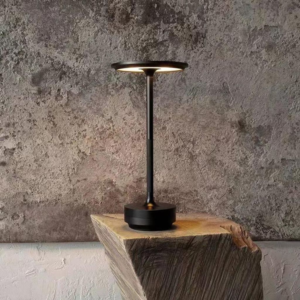 A black LED table lamp is placed on a wooden block against a textured gray wall.
