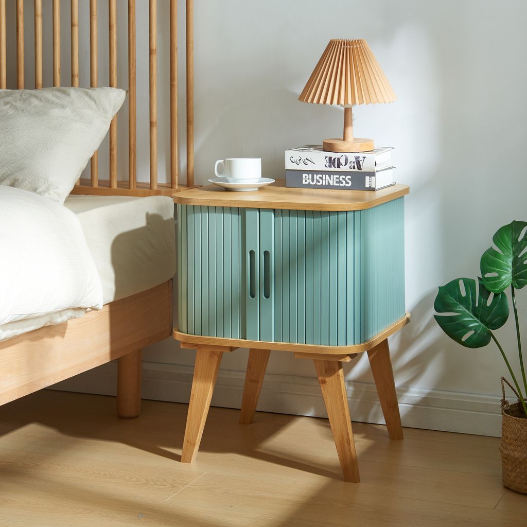 A bedside table next to a bed, with a lamp and books on top.