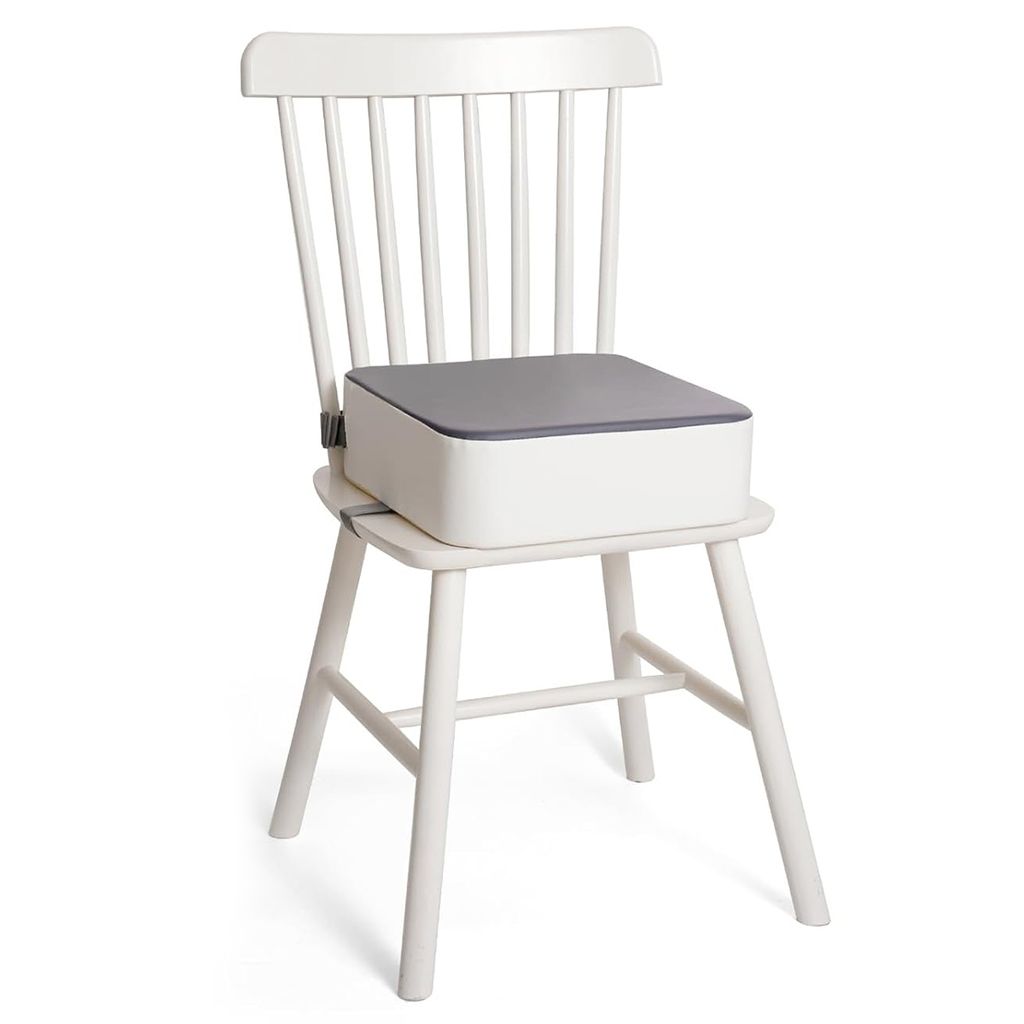 A white wooden chair with a white and gray booster seat for children placed on it.